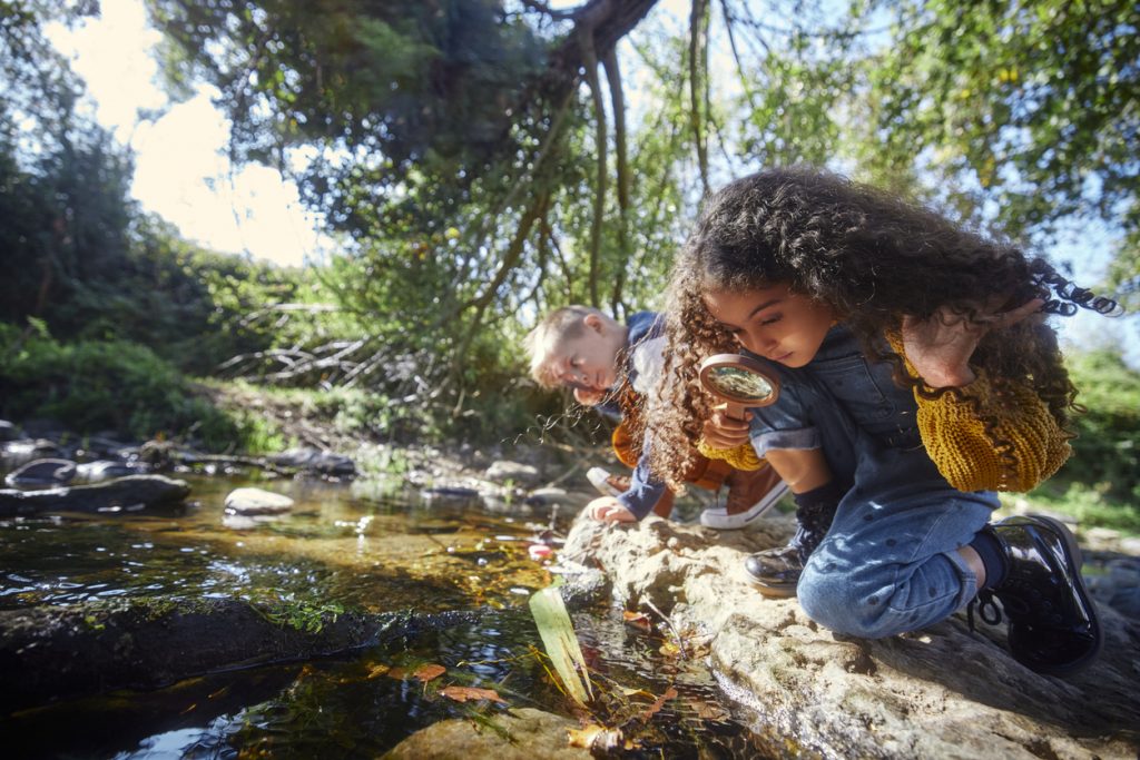 Small boy and girl looking at river with magnifier