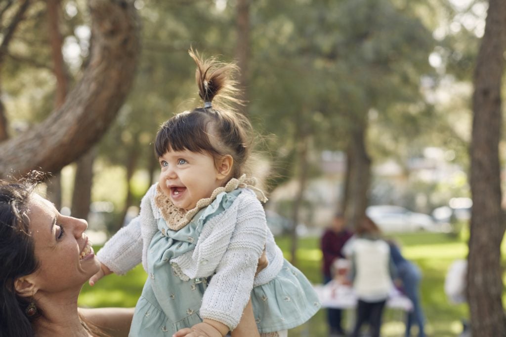 Cute little girl enjoying playing on her mother's lap in a park.